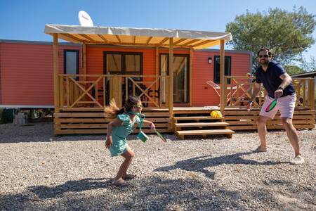 Father and daughter play tennis in front of a chalet at the RCN Domaine de la Noguière holiday park