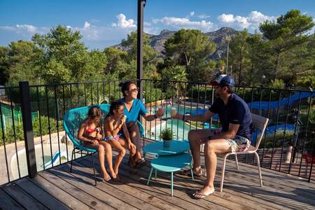 The family is sitting on the terrace by the outdoor swimming pool of RCN Domaine de la Noguière